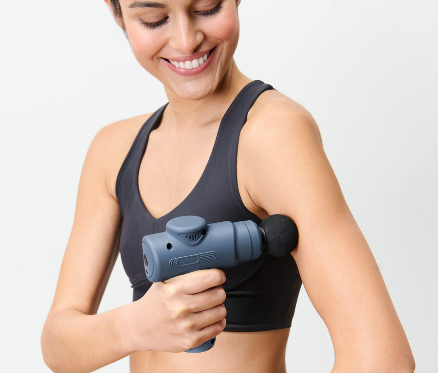 Nő mini masszázspisztolyt használ a karján.