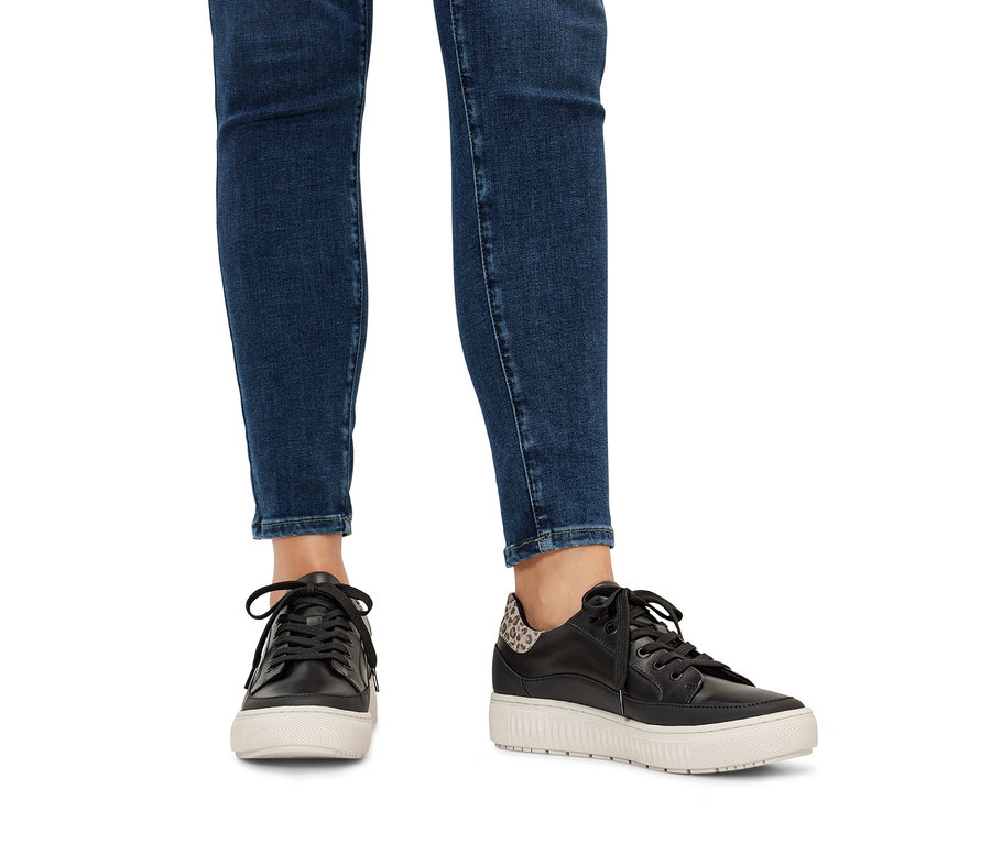 Farmerben lévő lábak és fekete/leopárdmintás női bőr sneaker cipő.