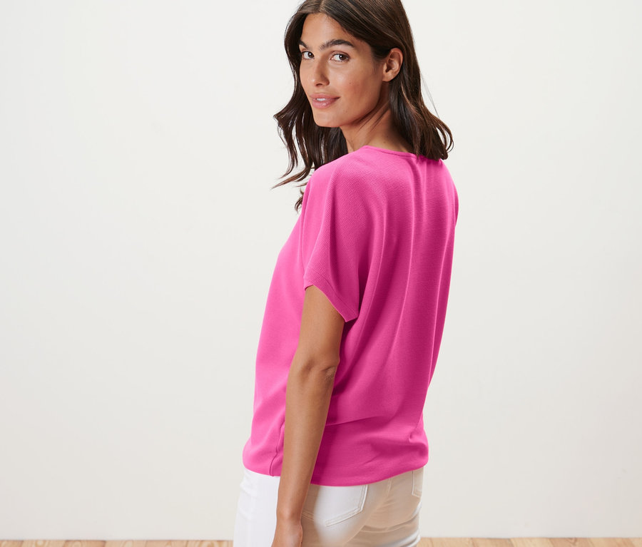 Egy nő a válla fölött néz, blúzt és fehér farmert visel.