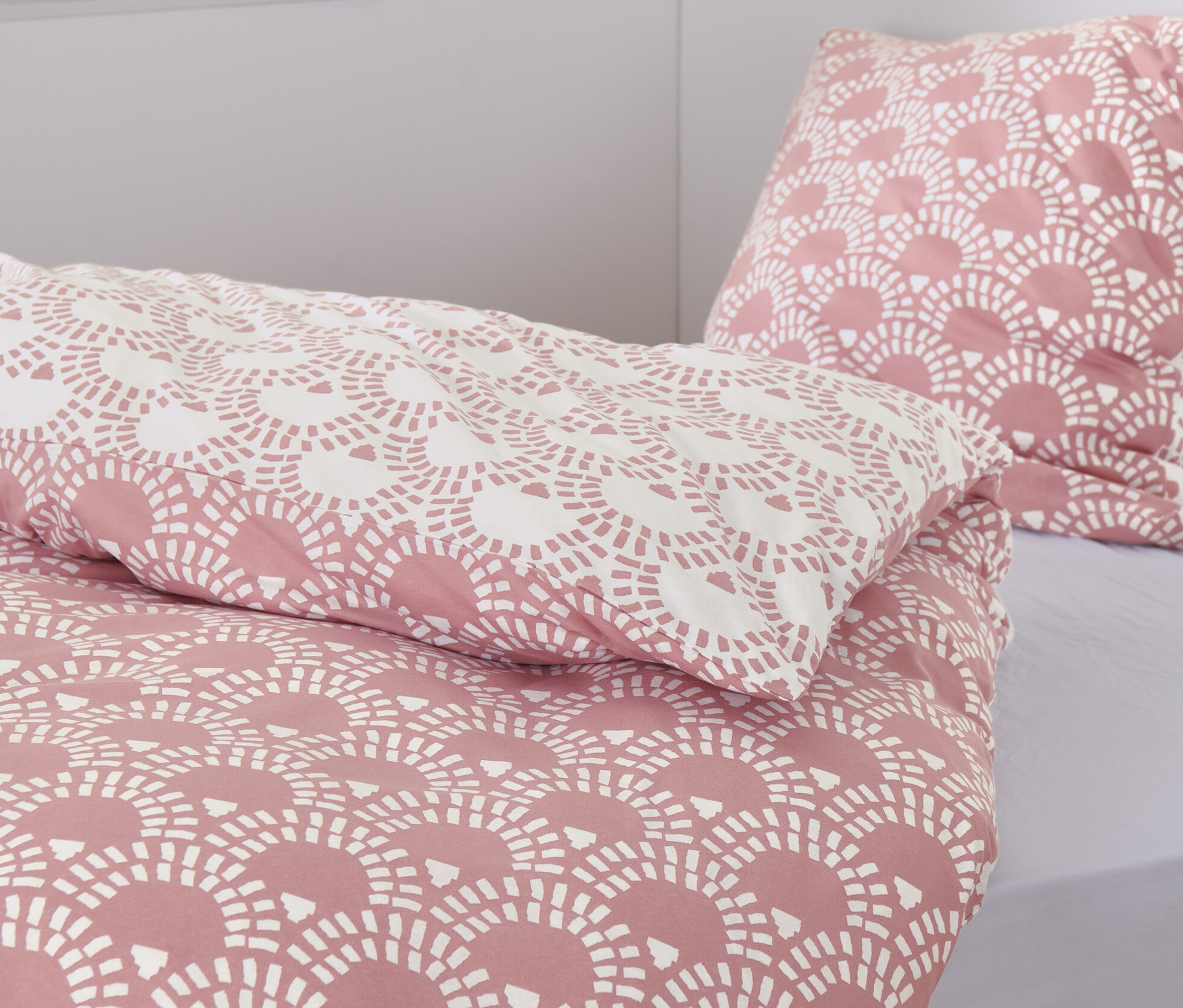 Közeli kép egy rózsaszín, mintás jersey ágyneműről. A háttérben két fonott kosár és könyvek láthatók.