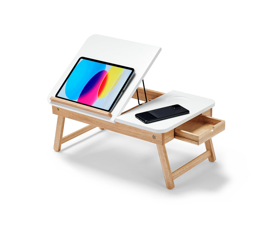 Egy fehér laptop ágyasztal világosbarna fa lábakkal. Az asztallapon egy tablet és egy mobiltelefon található.