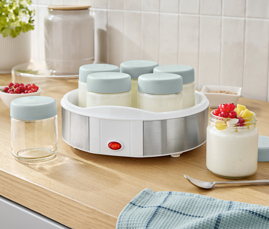 Joghurtkészítő hat üveggel és egy pohár joghurttal és gyümölcsökkel.