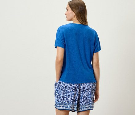 Hátulról pózoló nő kobaltkék lenvászon pólóban és kék-fehér rövidnadrágban.