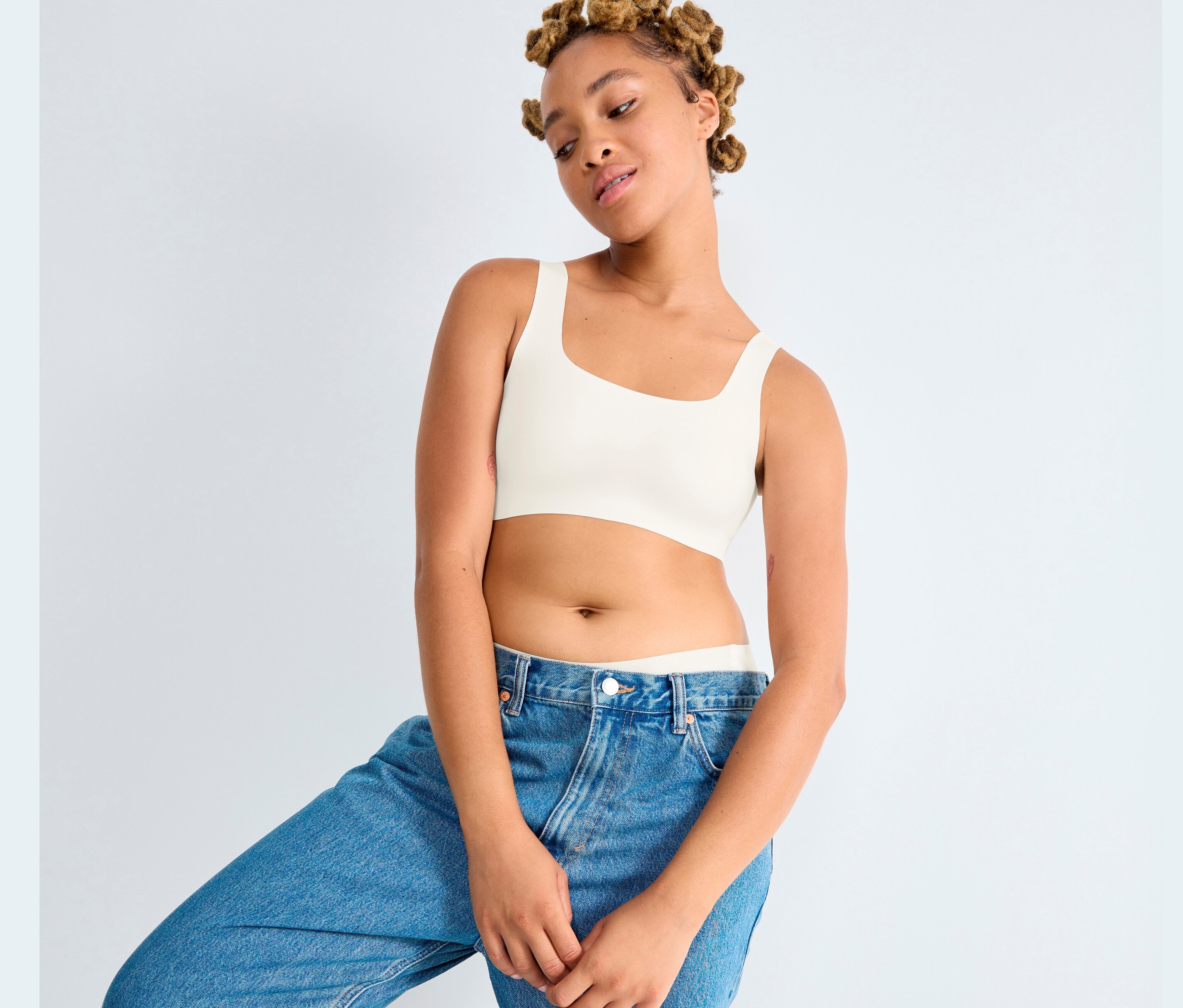 Fiatal nő pózol farmerben és selyemfehér Sloggi ZERO Feel 2.0 topban.