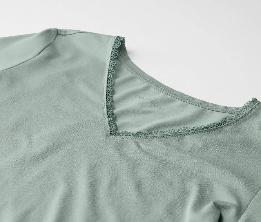 Egy világoszöld, rövid ujjú, csipkével szegélyezett V-nyakú póló részlete.