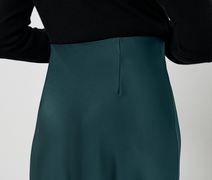 Hátulnézet egy fekete blúzt és zöld szoknyát viselő nőről.