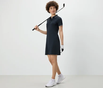 Nő golfütőt tart a vállán és sportruhát visel.