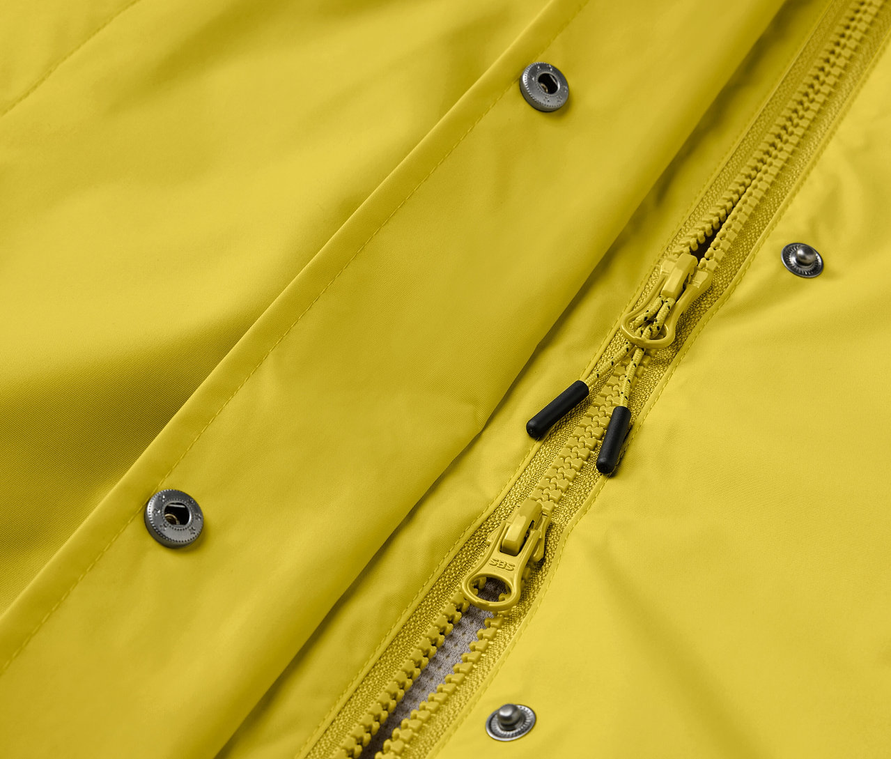 Egy sárga kabát részlete ezüst patentokkal és sárga cipzárral.