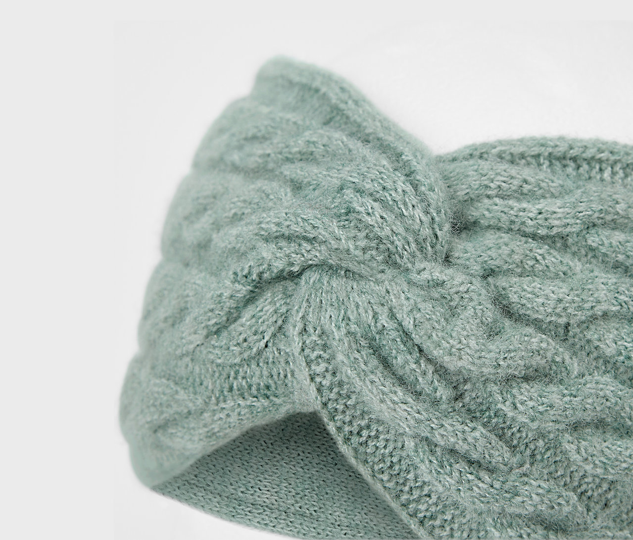 Egy világoskék, kötött fejpánt közeli képe, fonott mintával.