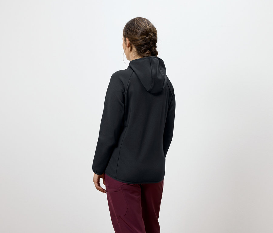 Hátulnézet egy barna hajú, fonott hajú nőről, aki fekete kapucnis pulóvert és bordó nadrágot visel.