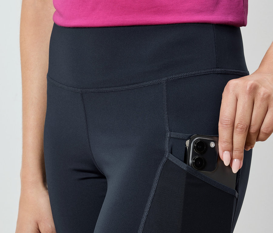 Nő okostelefont tesz a tengerészkék leggings zsebébe.