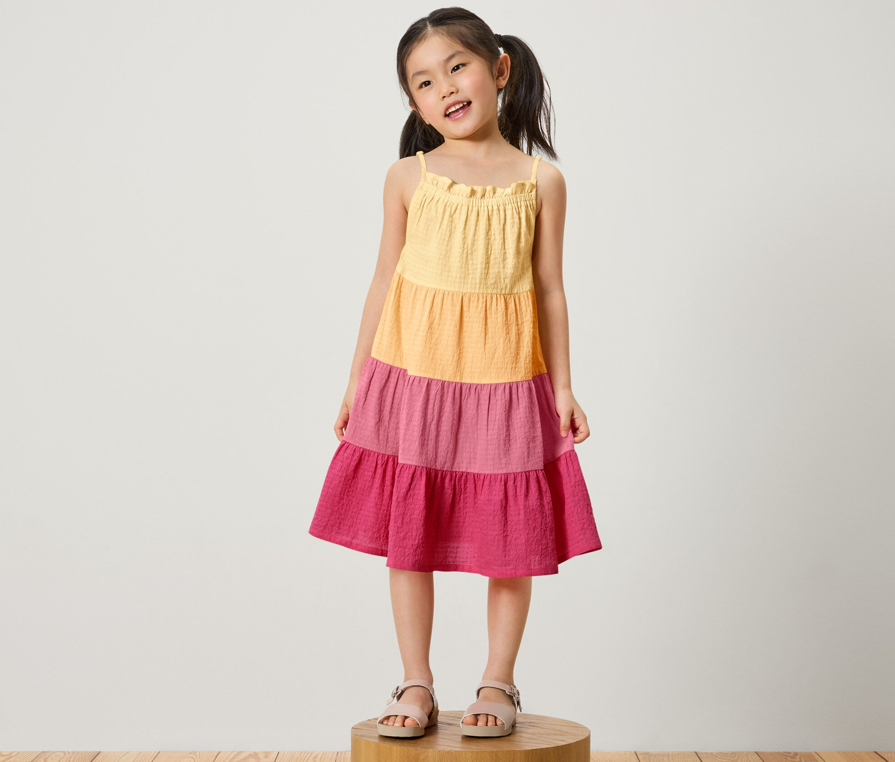 Egy lány áll egy fa talapzaton és szövött gyerekruha van rajta.