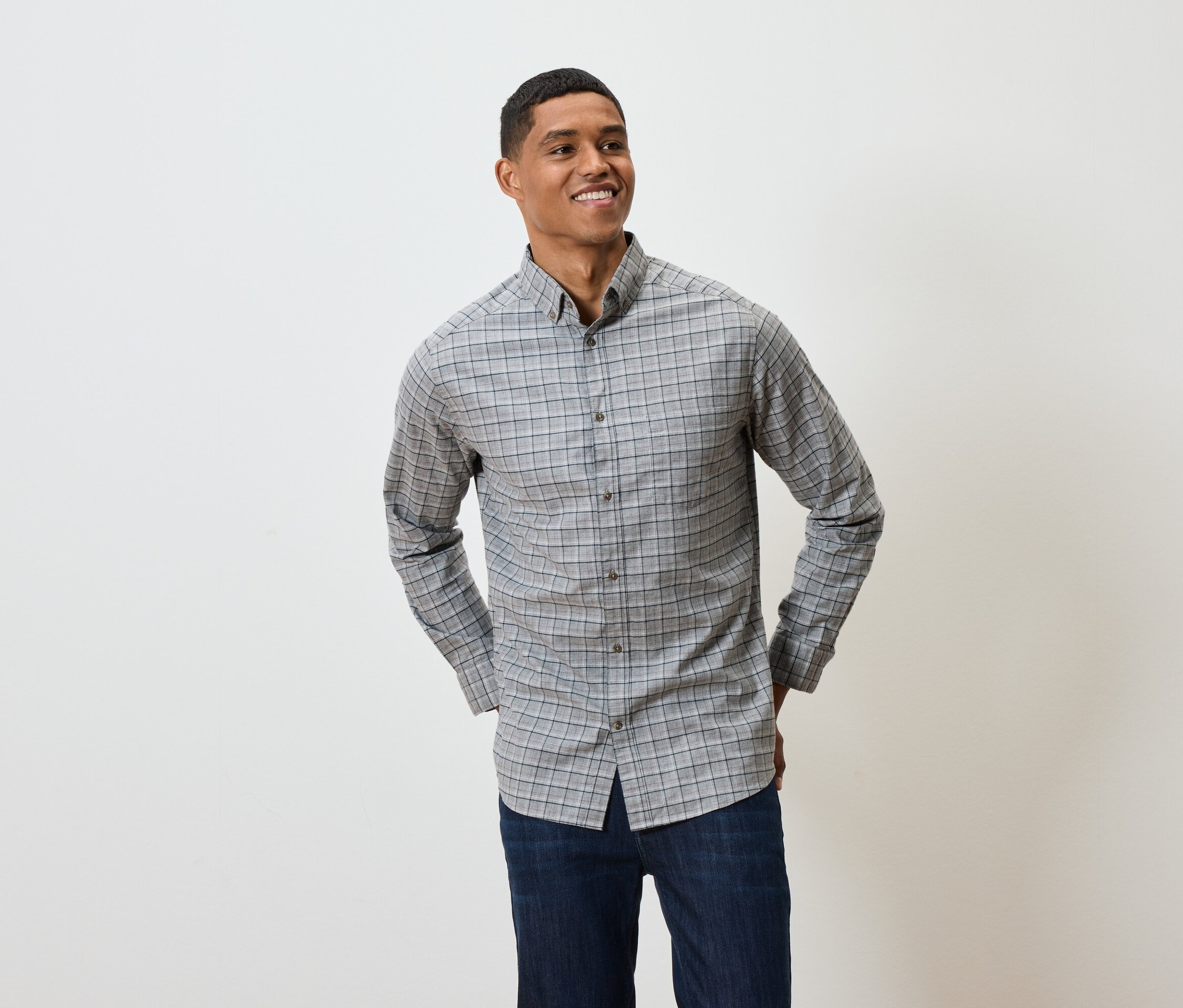 Mosolygó férfi szürke kockás, hosszú ujjú ingben és sötétkék farmerben pózol.