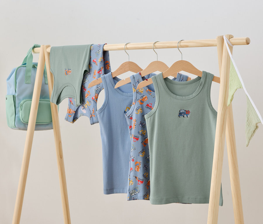 Gyermekruhák lógnak egy fa állványon, köztük atléták és egy hátizsák.