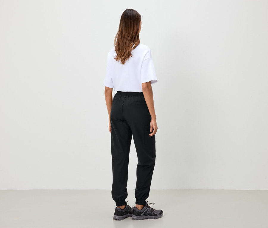 Egy nő áll háttal, fehér pólót, fekete nadrágot és szürke cipőt visel.