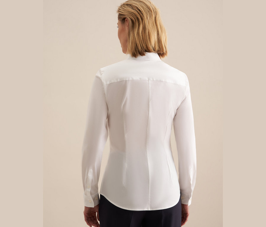 Hátulnézet egy rövid szőke hajú nőről, aki fehér Seidensticker slimfit blúzt és sötétkék nadrágot visel.