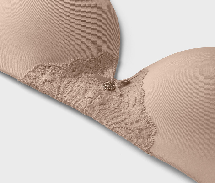 Egy bézs színű melltartó közeli képe, csipkés szegéllyel és egy kis díszgombbal.