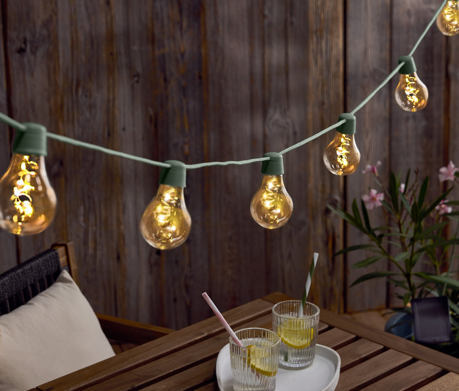 Izzós fényfüzér lóg egy faasztal fölött, italokkal és egy kalappal.