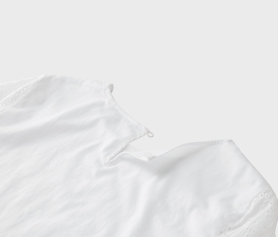 Egy fehér blúz részletfotója, hímzett lyukakkal az ujján.