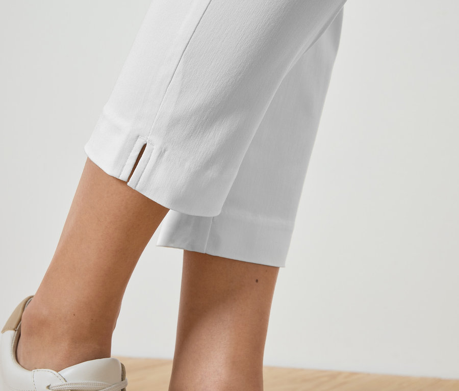 Közeli kép egy fehér nadrágot és hozzáillő tornacipőt viselő személy lábairól.