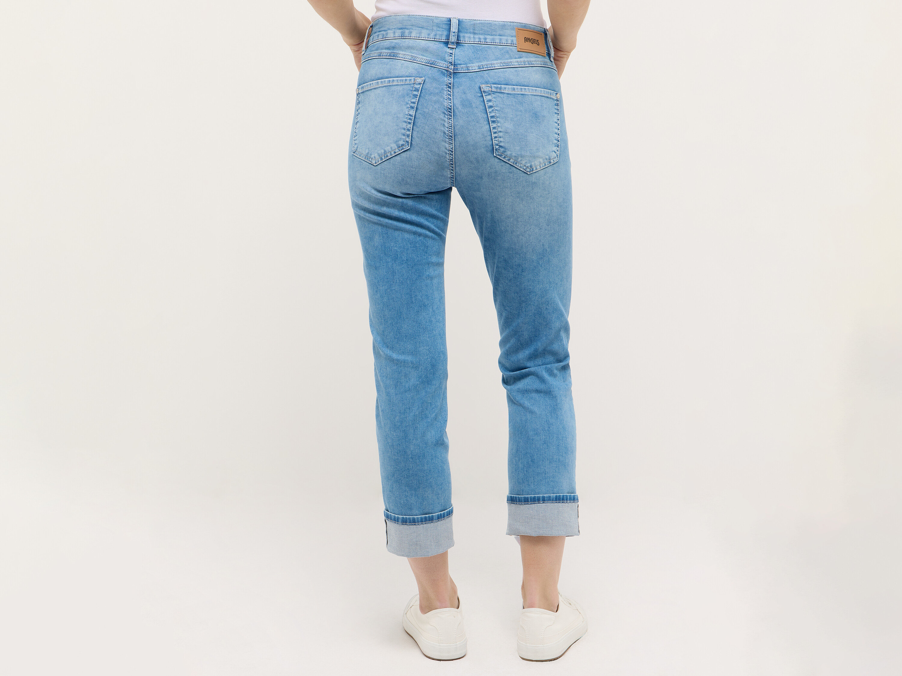 Egy nő csípője és lábai világoskék farmerben és fehér tornacipőben, hátulról fényképezve.