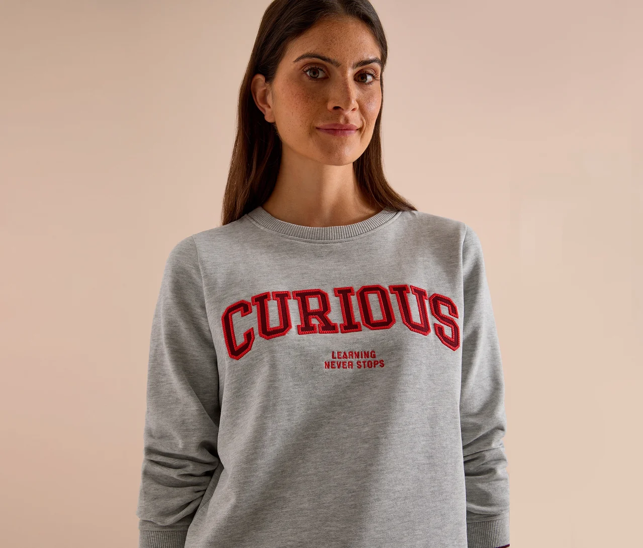 Nő visel egy szürke CECIL szabadidőfelsőt piros "CURIOUS" és "LEARNING NEVER STOPS" felirattal.