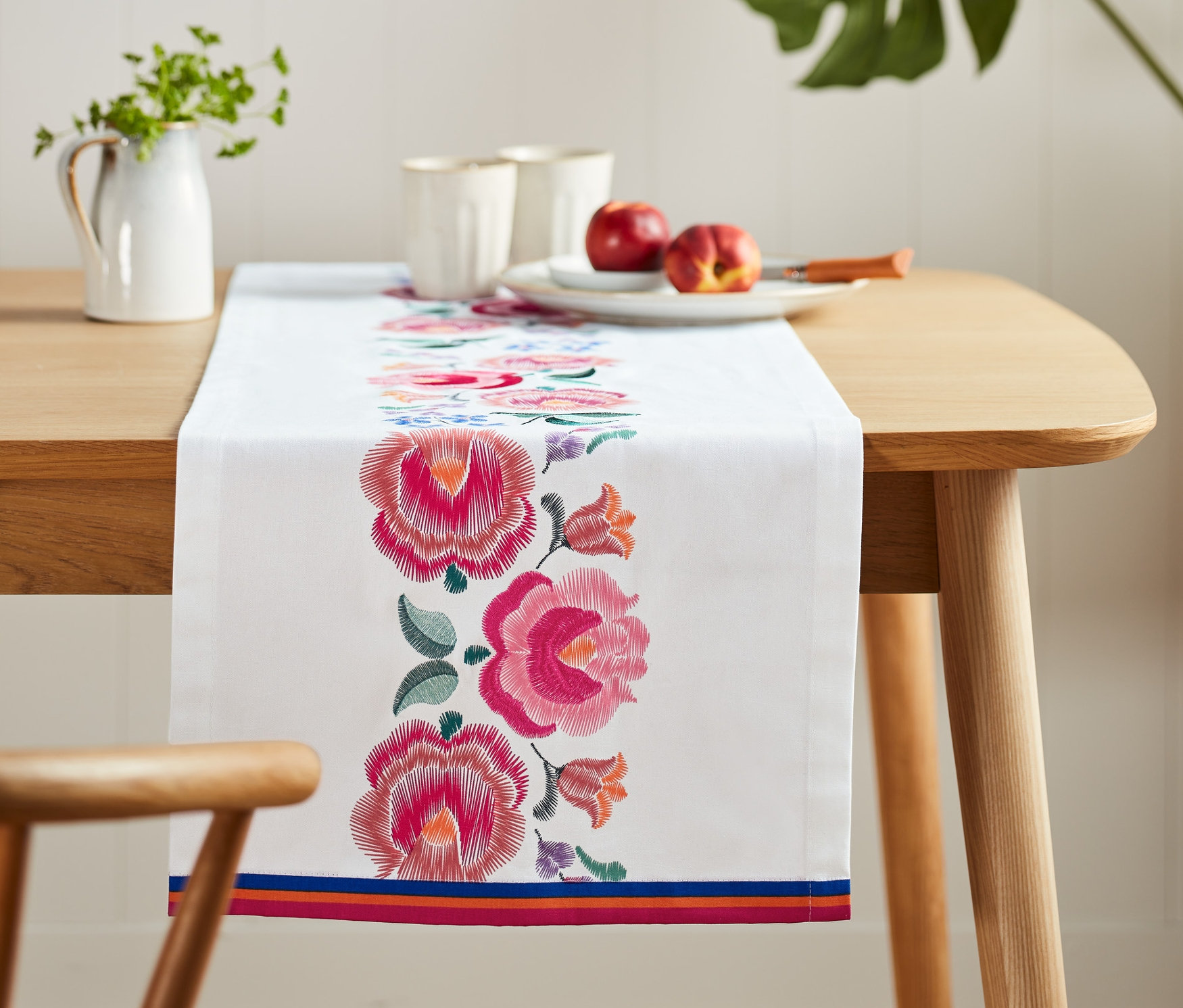 A fa asztalon egy fehér, hímzett virágos asztali futó fekszik.