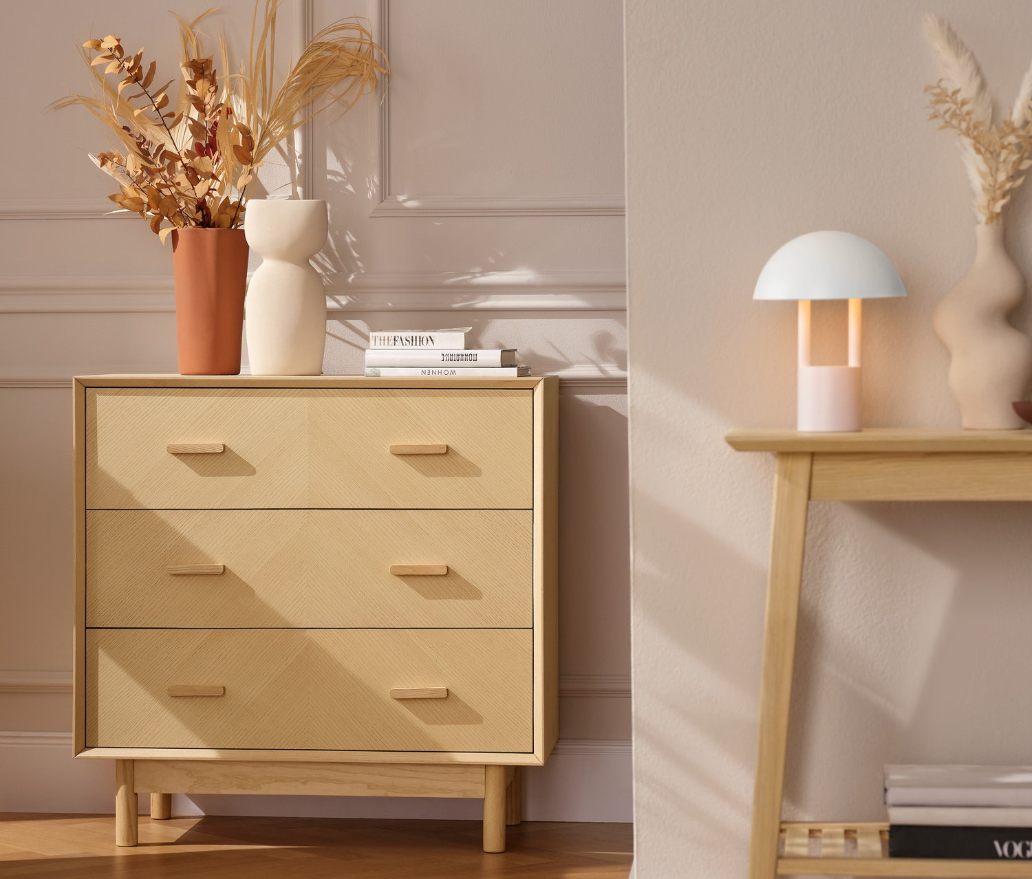 Egy kőris komód 3 fiókkal egy szürke fotel mellett, narancssárga takaróval.