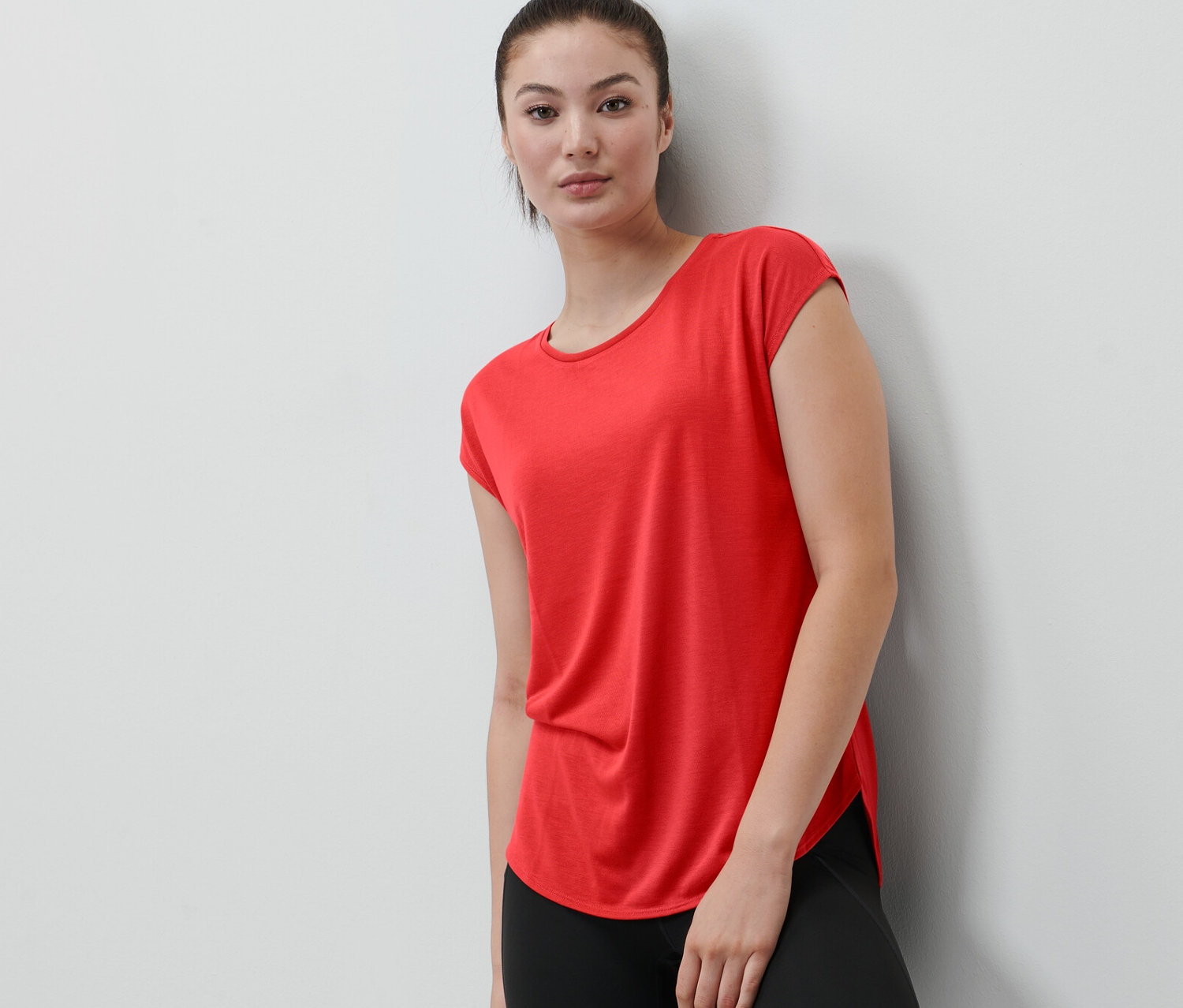 Egy falnak támaszkodó nő piros sportfelsőt visel.