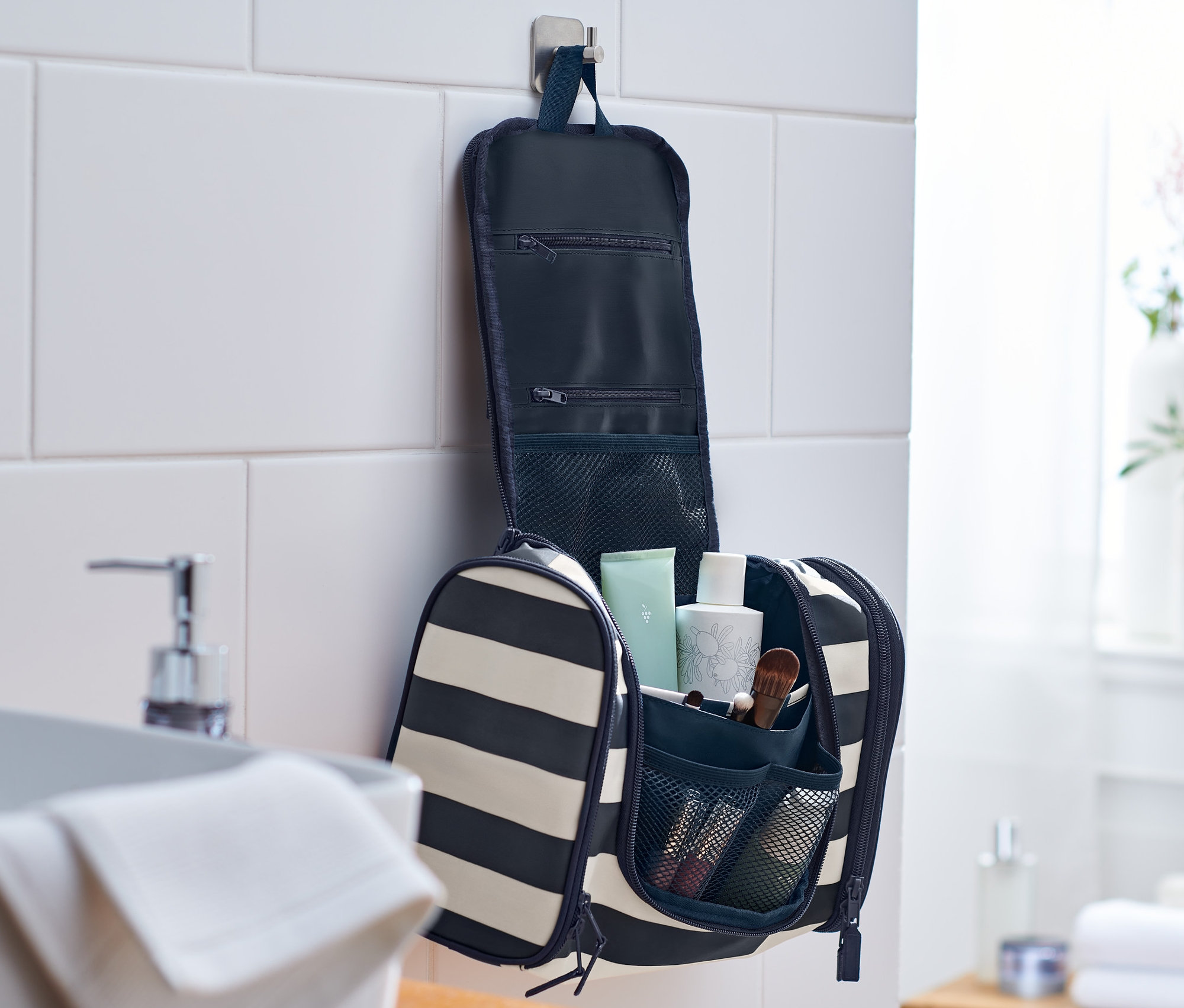 Egy csíkos kozmetikai táska nyitva lóg egy fürdőszoba falán.