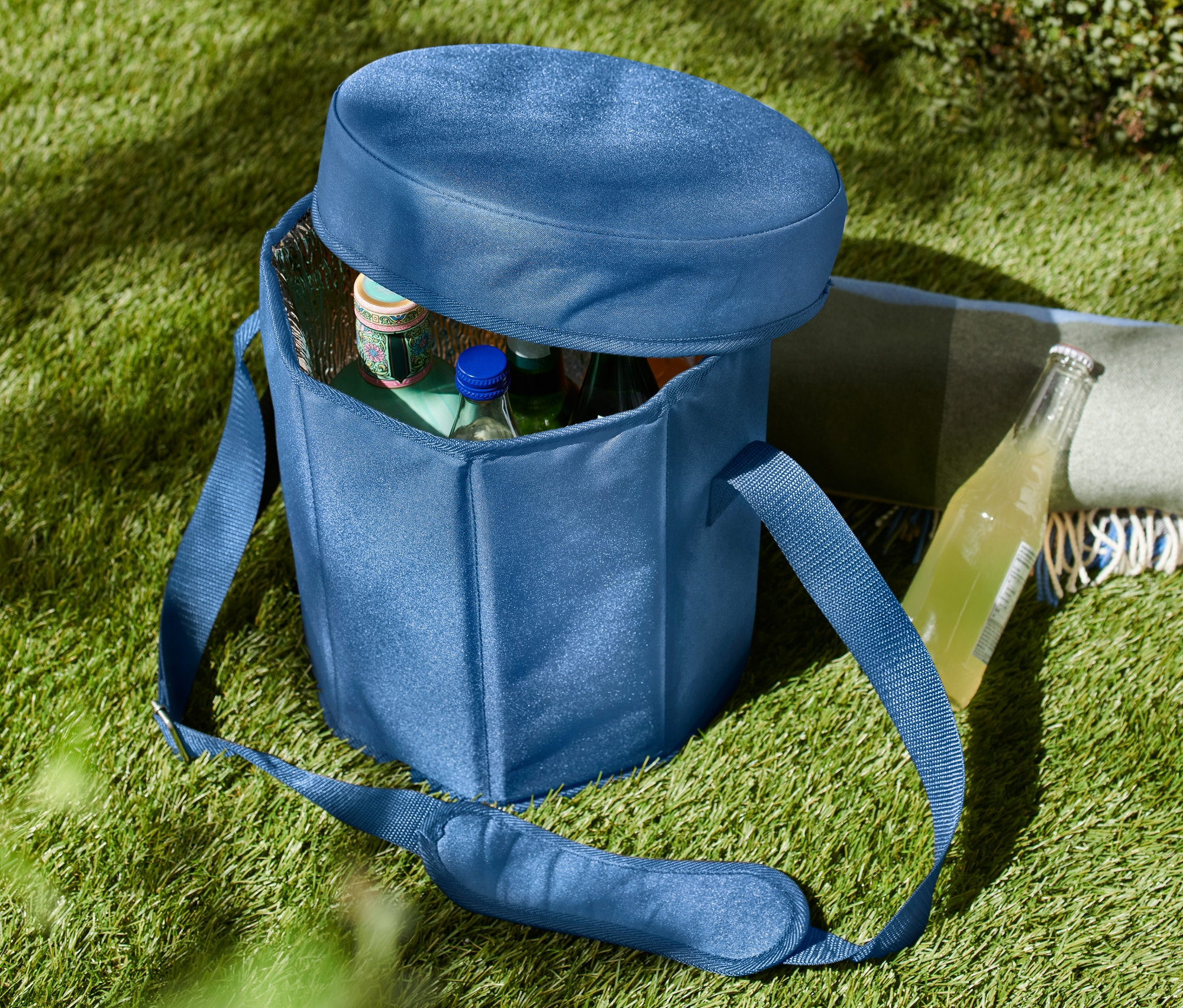 Egy kék 2 az 1-ben hűtőtáska a füvön, részben nyitva, benne palackokkal.