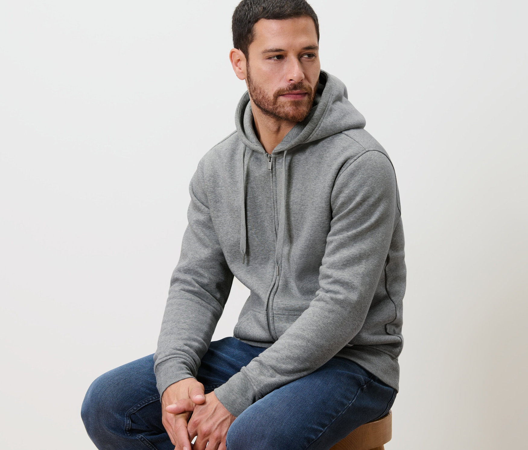 Férfi ül egy széken, szürke kapucnis szabadidőfelsőt visel.