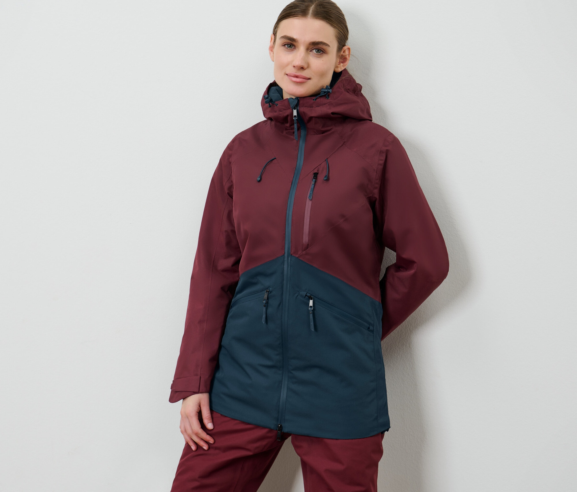 Nő pózol női sí- és snowboardkabátban, bordó/sötétkék színben.