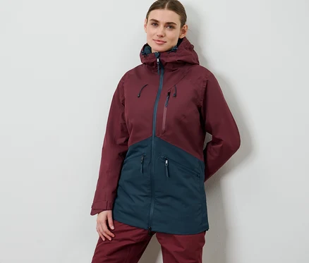 Nő pózol női sí- és snowboardkabátban, bordó/sötétkék színben.