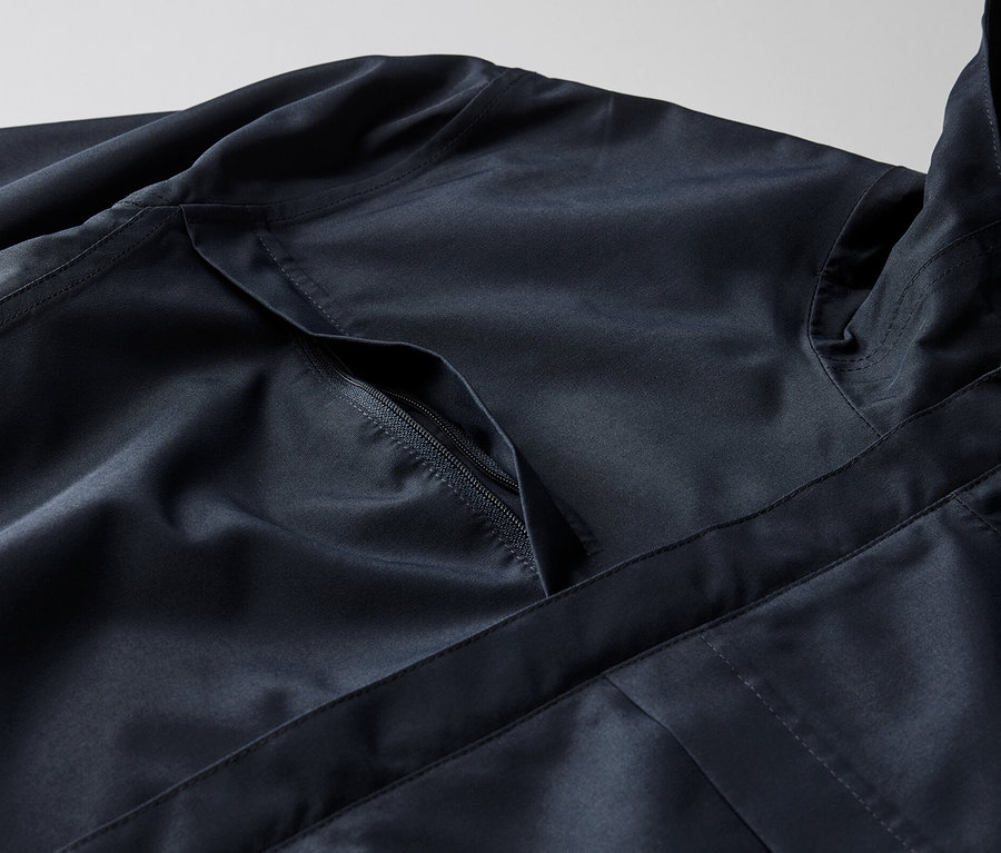 Egy sötétkék férfi funkcionális parka kabát részlete, cipzáras zsebbel.