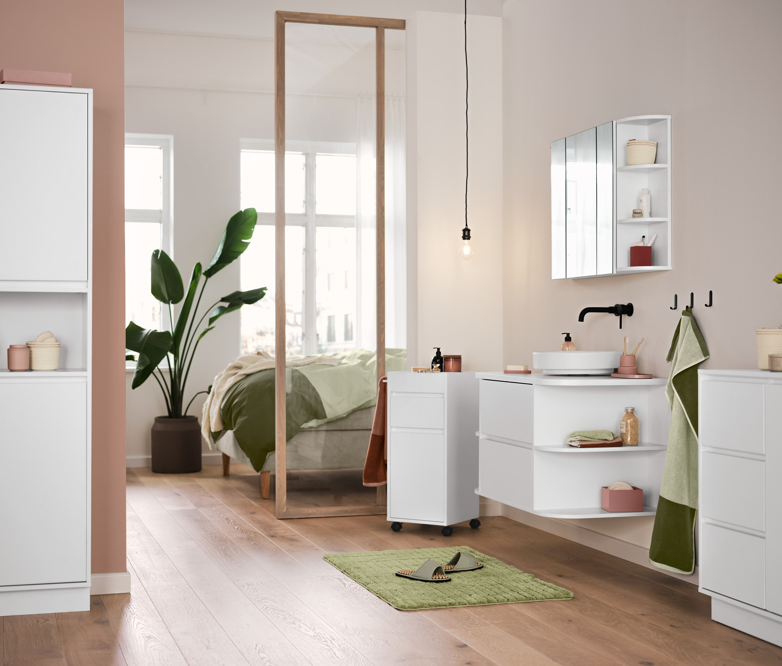 A fürdőszobában fehér fürdőszobabútorok, egy zöld Comfort kádkilépő és kiváló minőségű szürkésszöld-mohazöld jacquard törölközők láthatók.