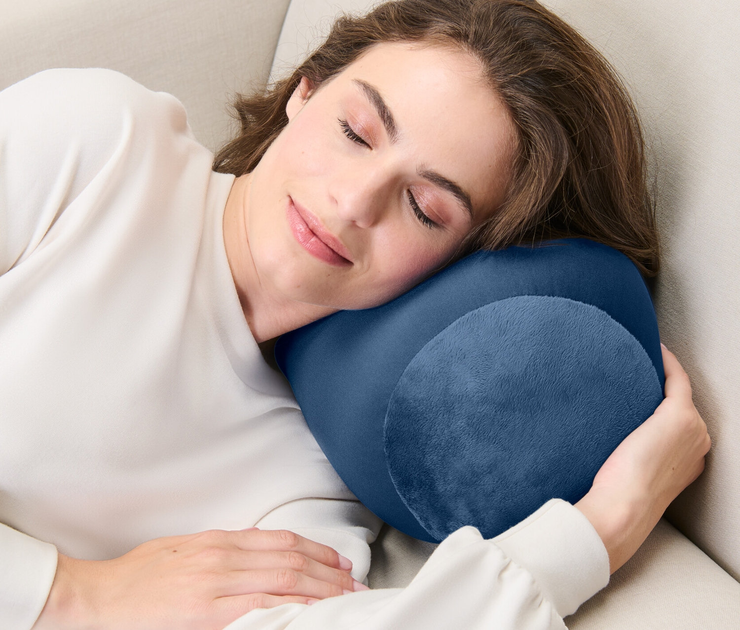 Egy nő alszik egy bézs kanapén egy sötétkék relaxációs párnával.