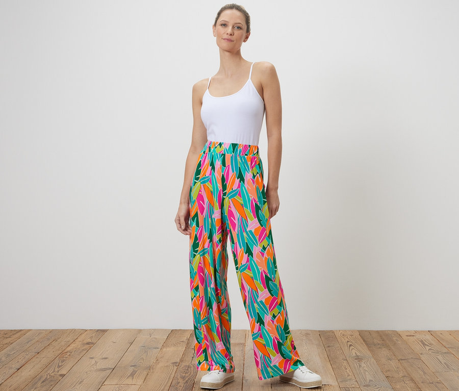 Egy nő áll, és nyomott mintás, színes palazzo nadrágot visel.
