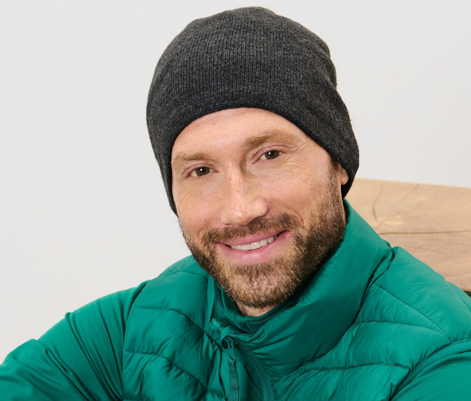 Szakállas férfi mosolyog, kötött sapkát és zöld mellényt visel.
