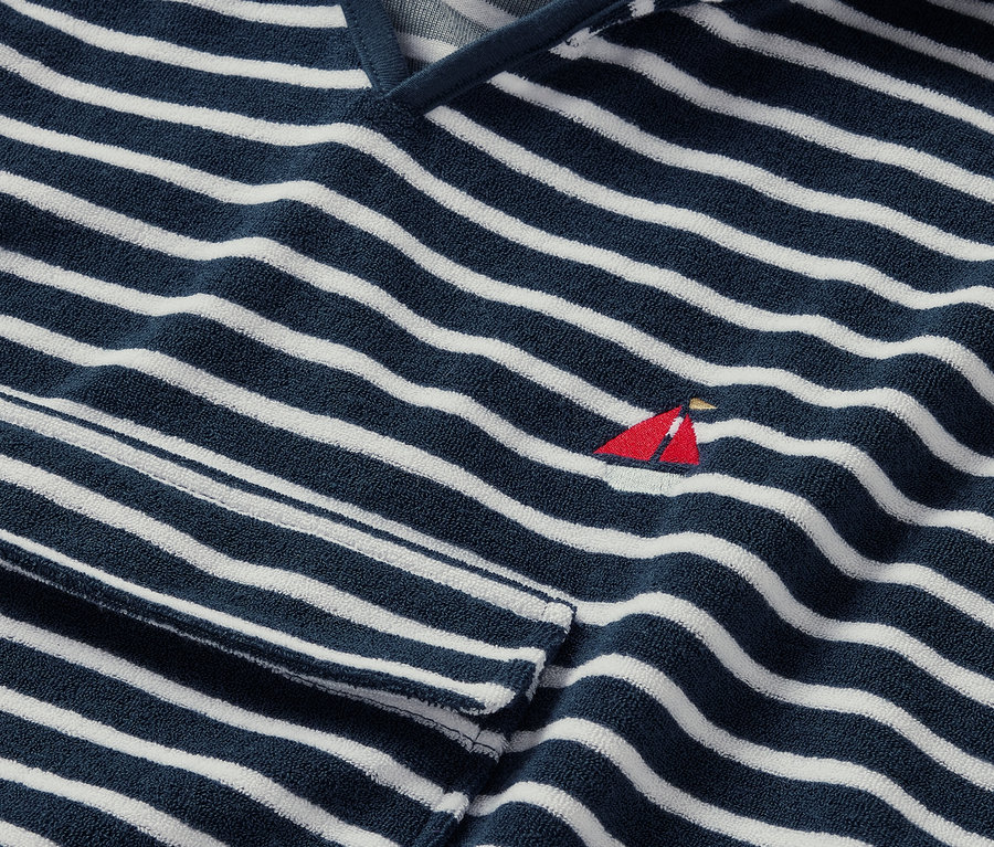 Egy sötétkék-fehér csíkos, kis vörös vitorlás hímzéssel ellátott kisgyerek frottírponcsó részlete.