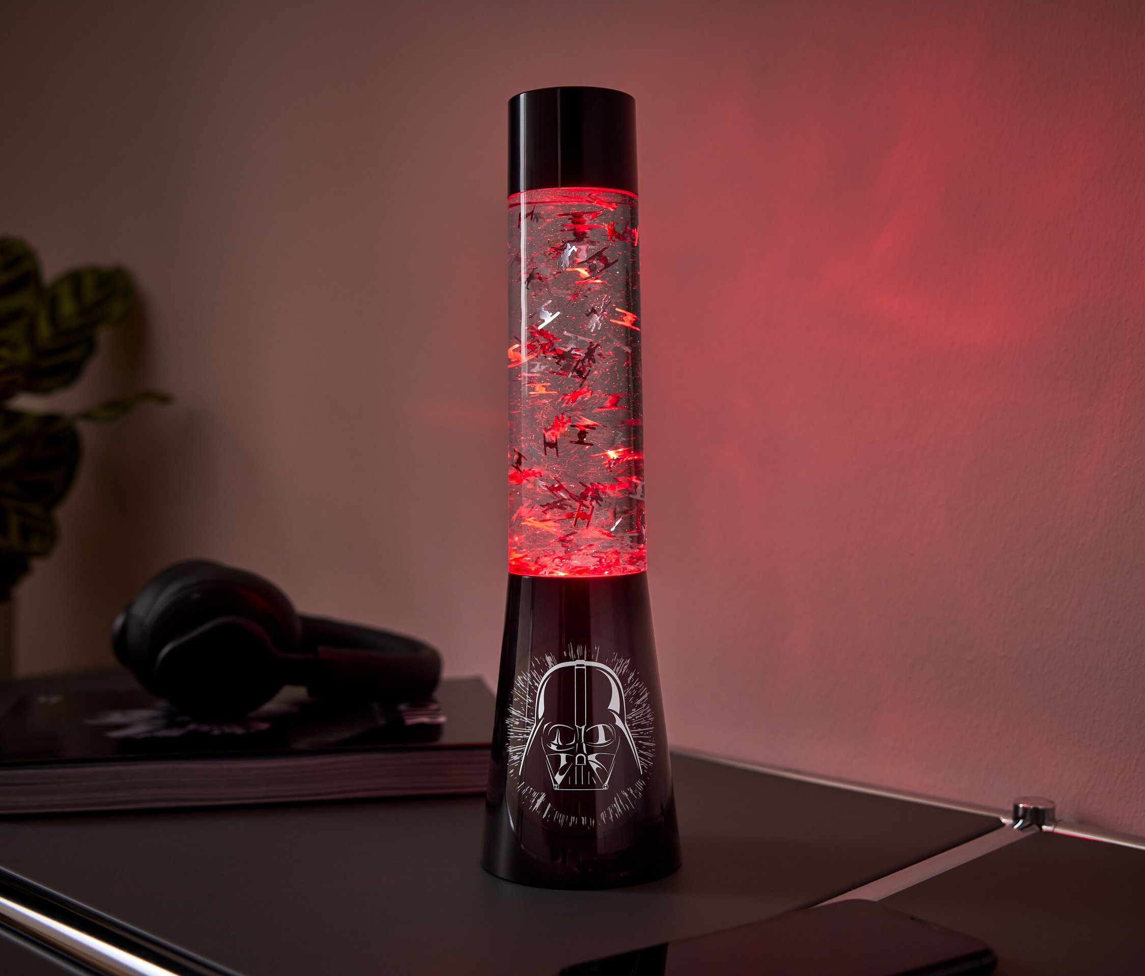 Egy fekete lávalámpa Darth Vader mintával az alján és piros csillámokkal a belsejében egy asztalon áll.