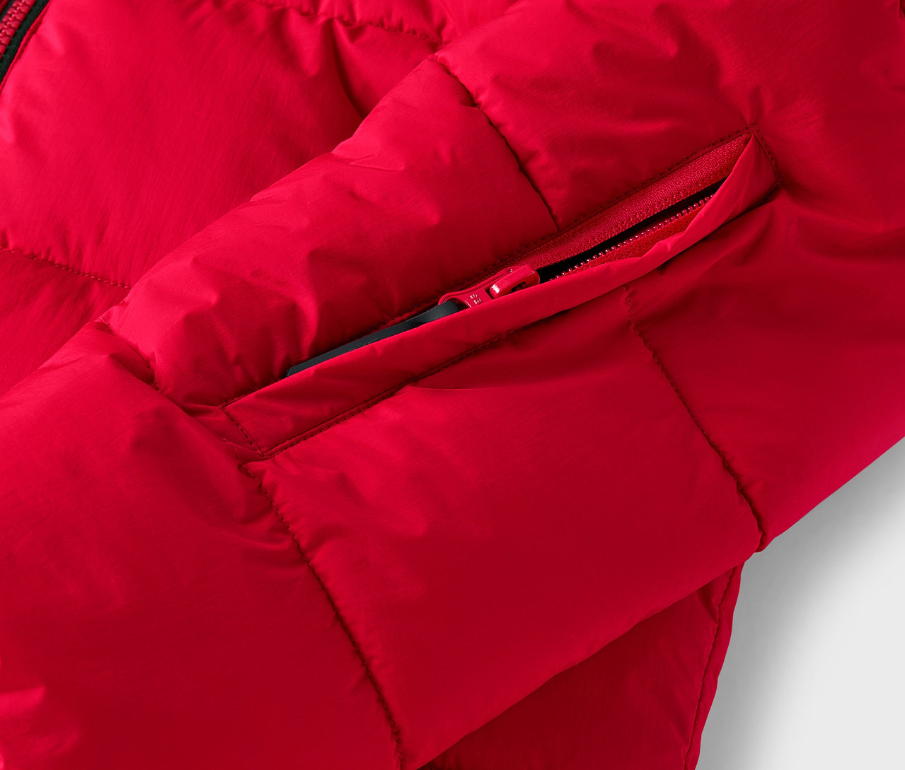 Egy piros, steppelt kabát részlete, cipzáros zsebbel.