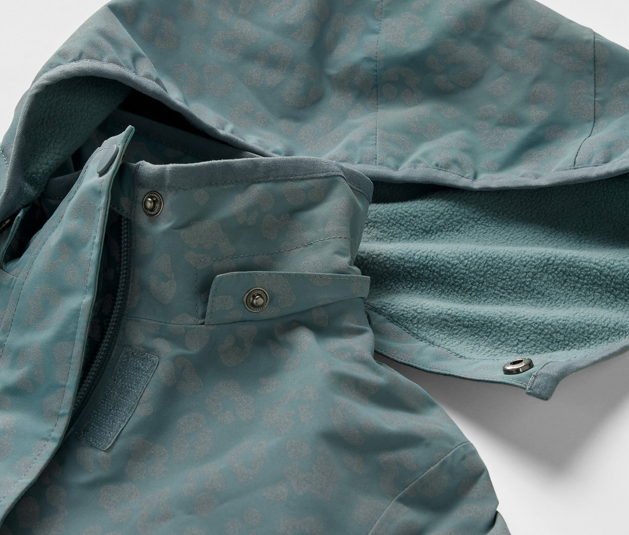 Egy gyerek termo esőkabát részlete fényvisszaverő elemekkel. A kabáton kapucni és cipzár található.