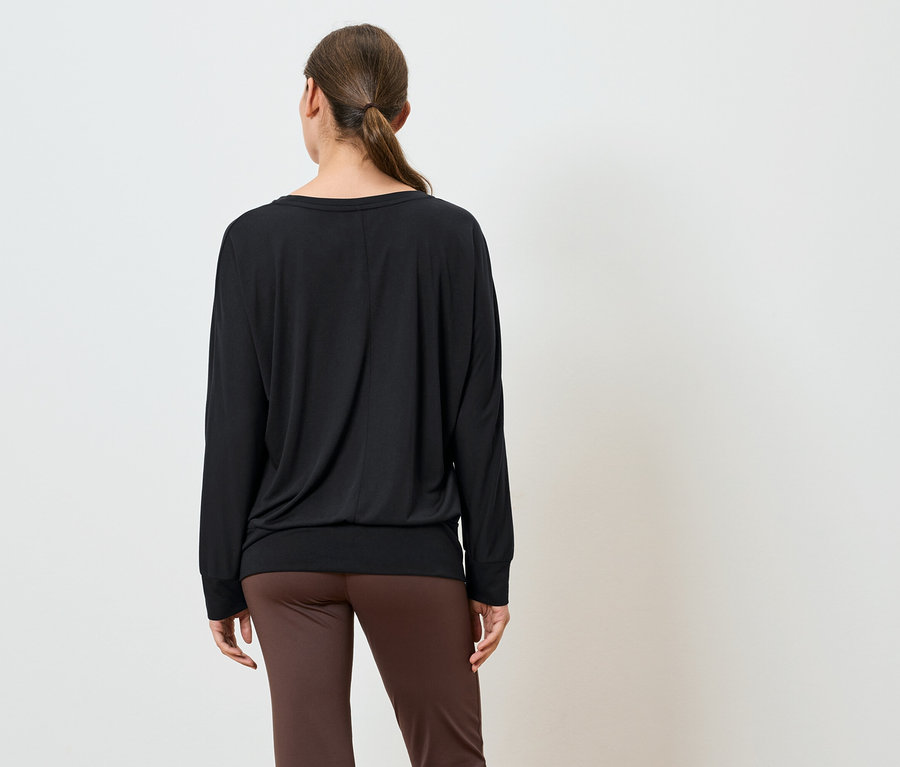 Hátulról álló nő fekete, hosszú ujjú felsőt és barna nadrágot visel.