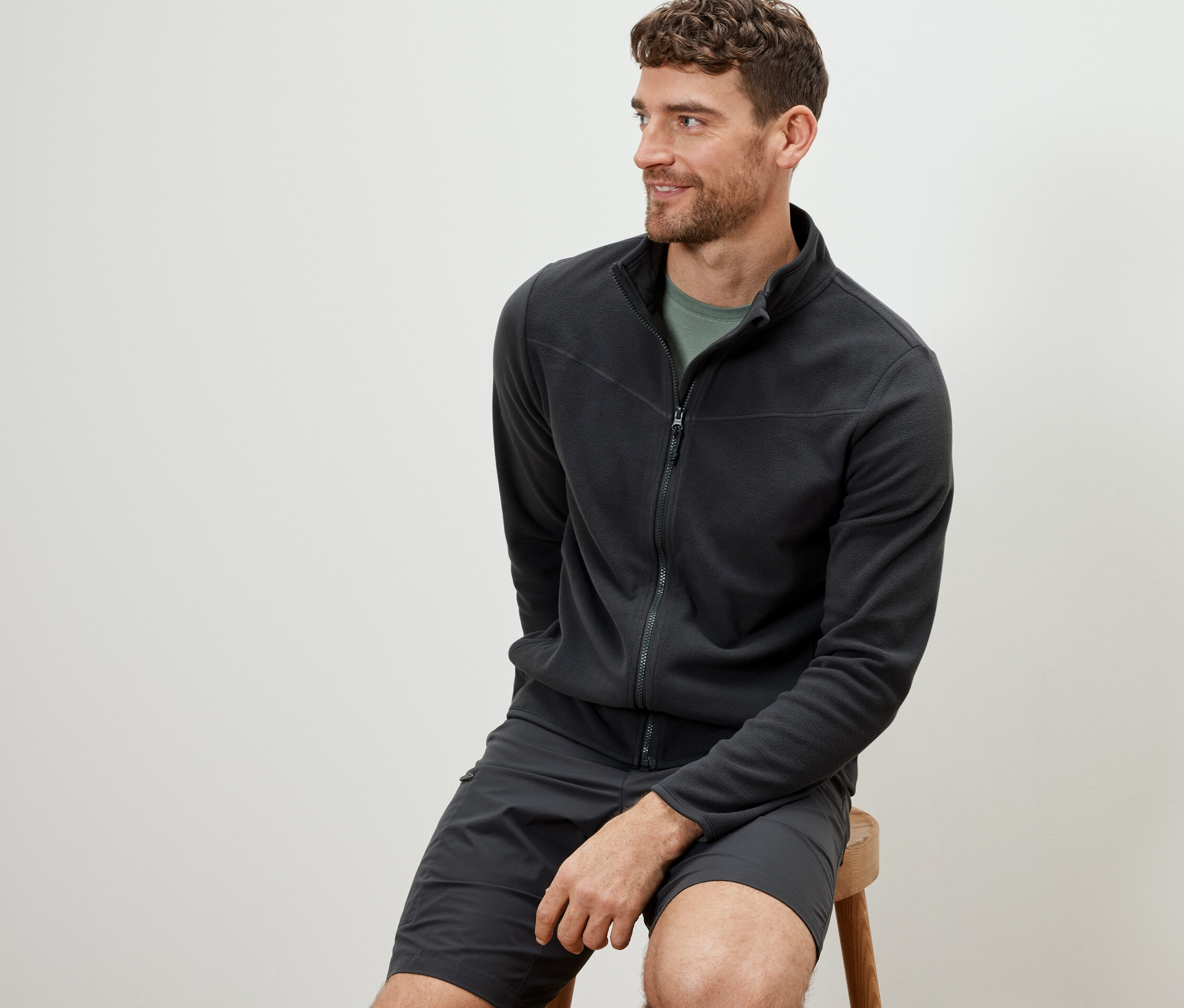 Egy férfi ül egy széken, és antracit színű polárfelsőt visel.