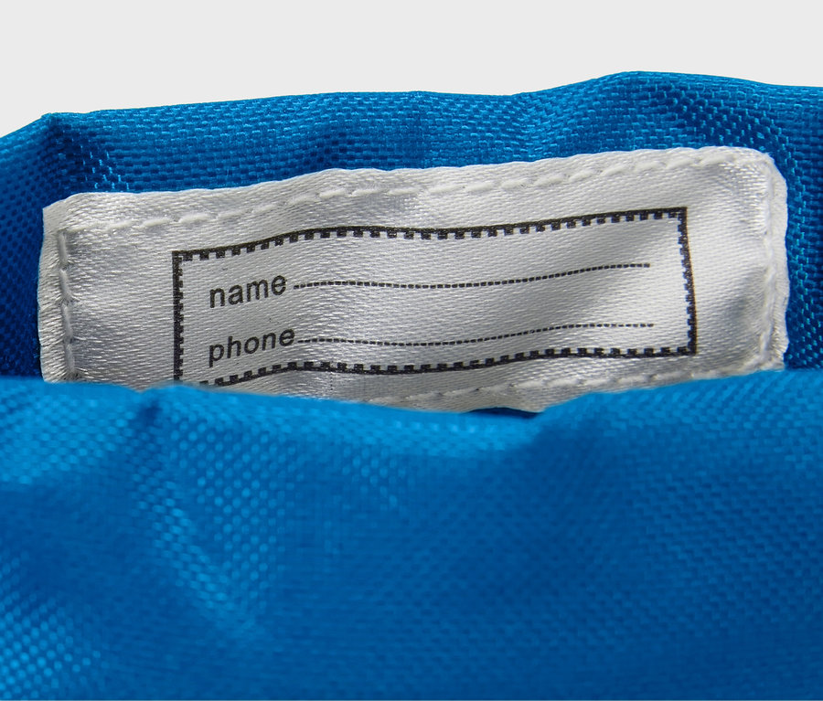 A kék anyagon egy fehér címke van rávarrva, fekete kerettel név és telefonszám számára.