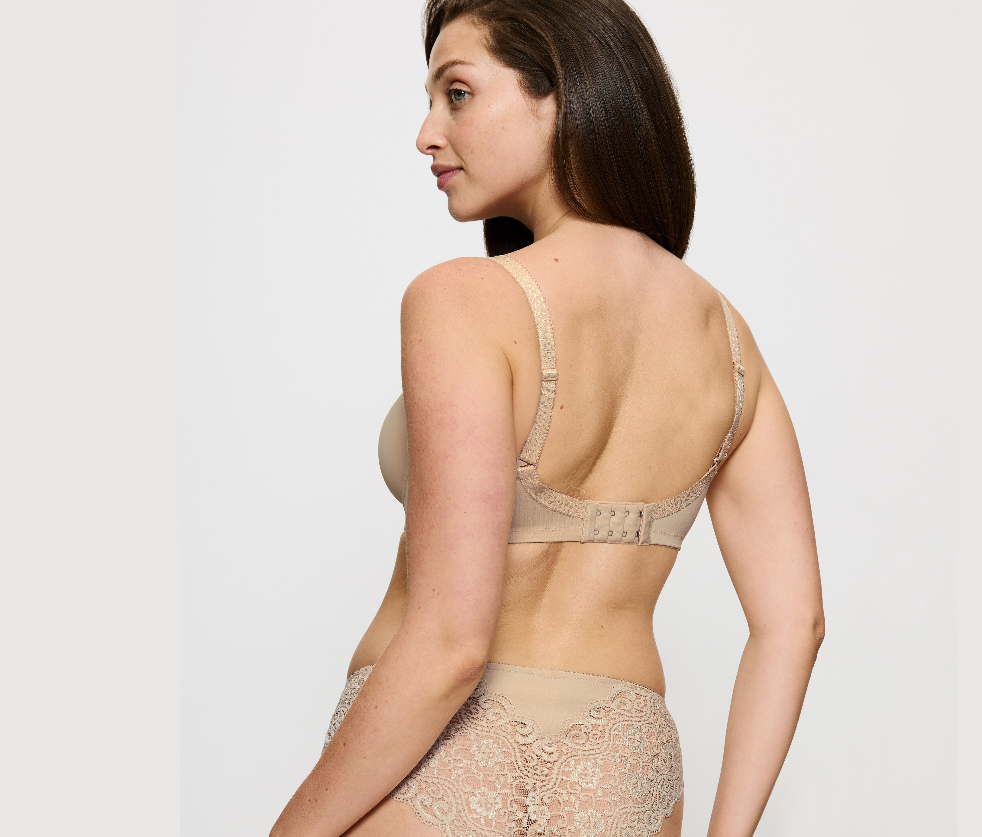Nő pózol Triumph Amourette kicsinyítő melltartóban, testszínűben és csipkés alsóban.