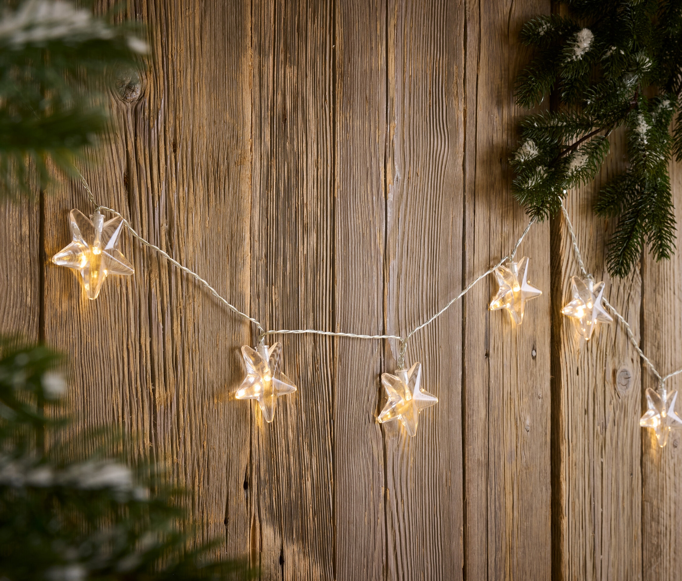 Egy csillag alakú fényfüzér lóg egy falon egy fenyőág mellett.