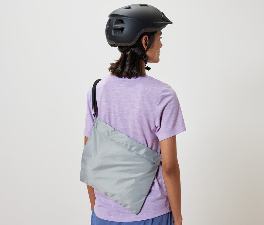 Kerékpáros sisakot viselő nő vállán kerékpáros bevásárlótáska van.