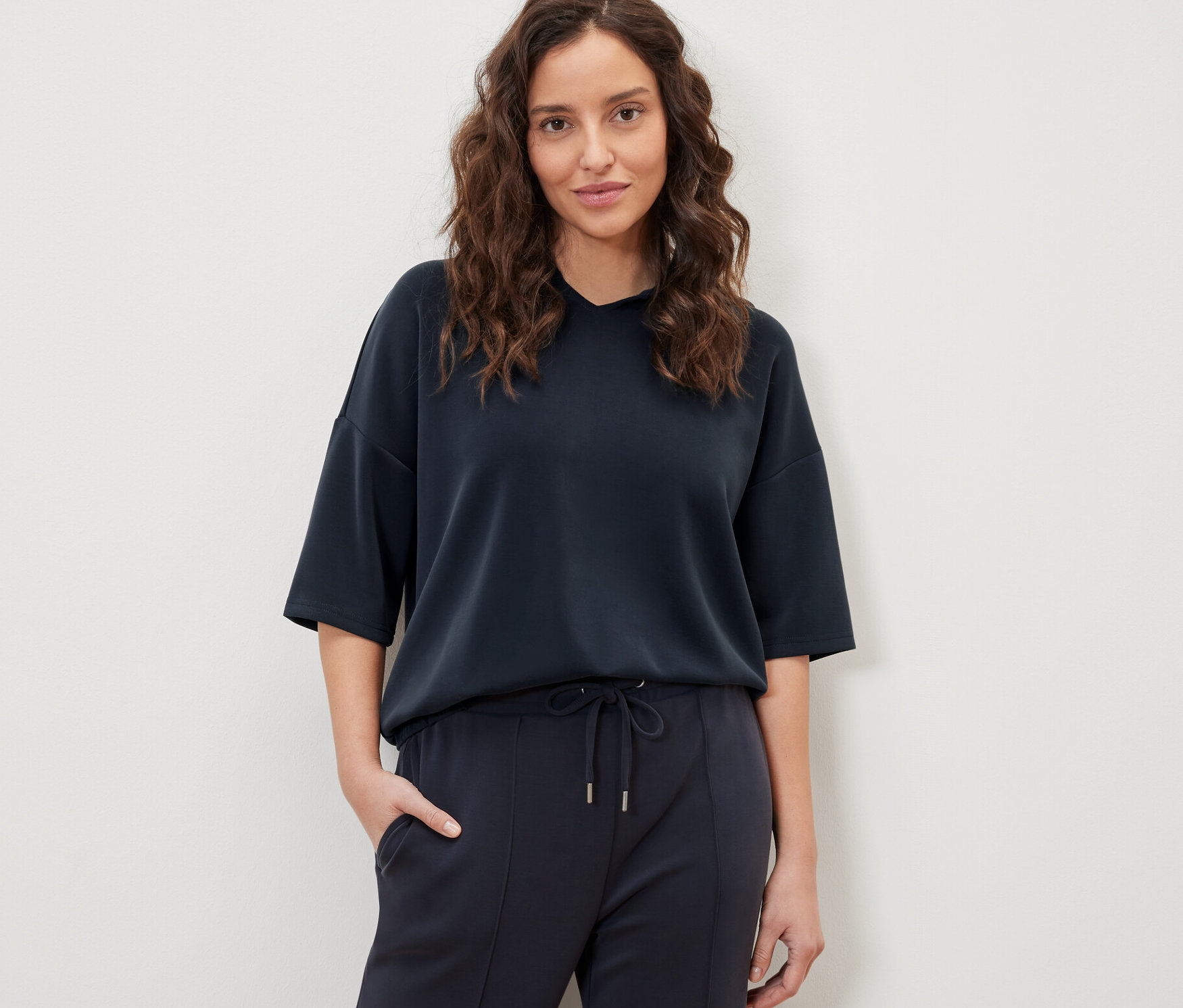 Nő pózol sötétkék, modálkeverék kapucnis felsőben és nadrágban.